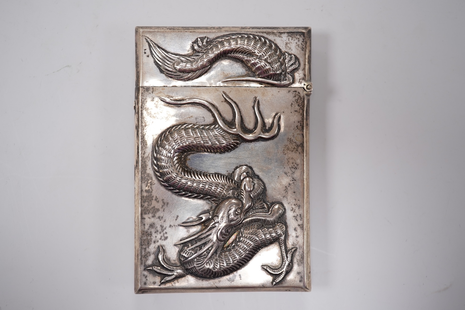 A late 19th century Chinese Export white metal card case, by Cum Shing, Canton, embossed with a dragon and applied shield shaped panel engraved with monogram, 90mm, 85 grams.